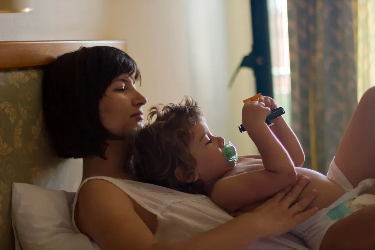 A parent lying beside a young child resting in bed