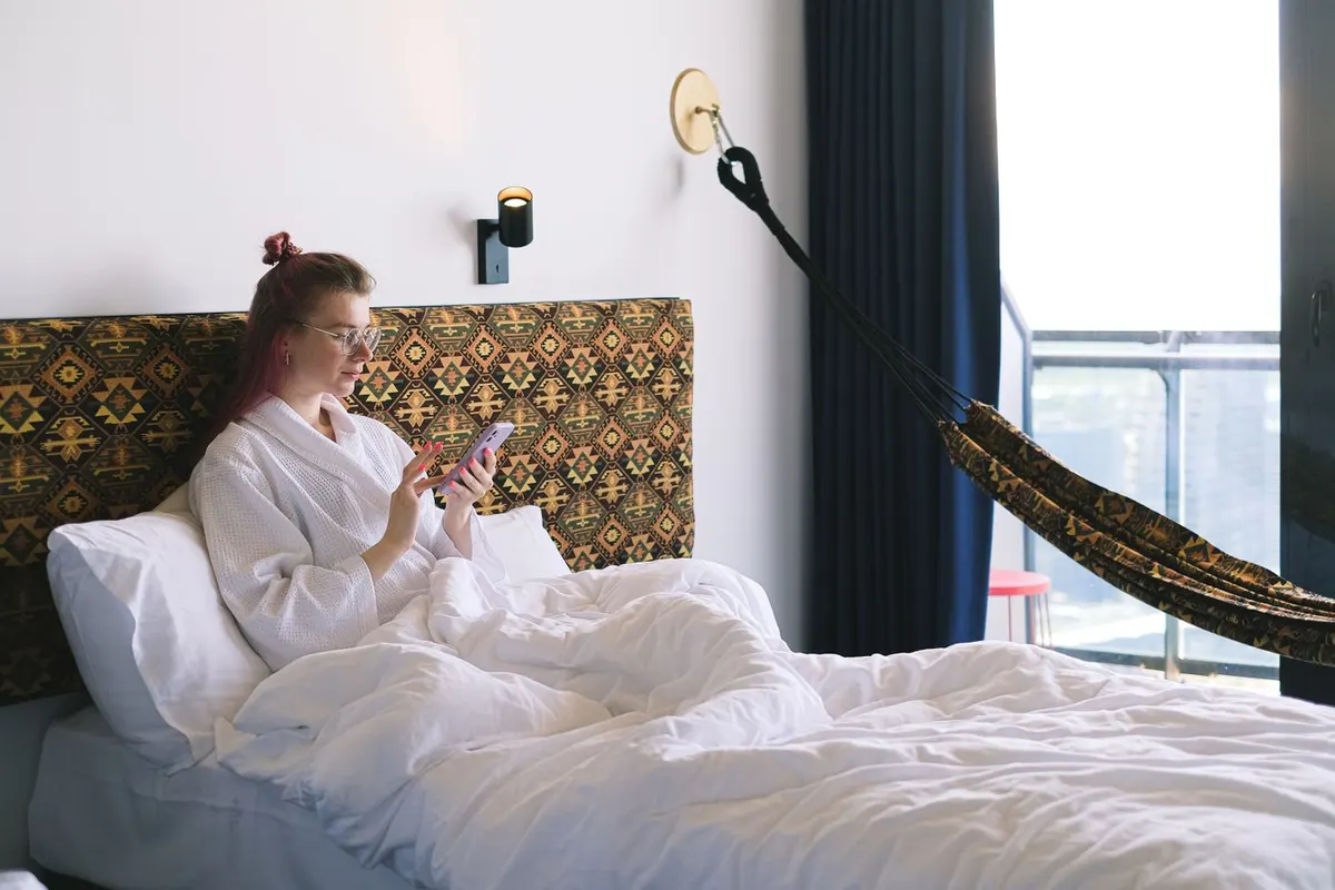 A traveler checking her phone from a hotel bed