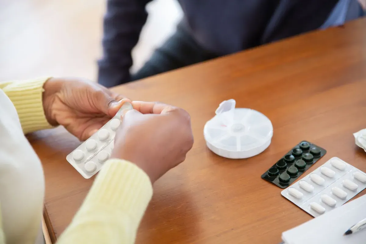 Hands sorting tablets from blister packs at a table